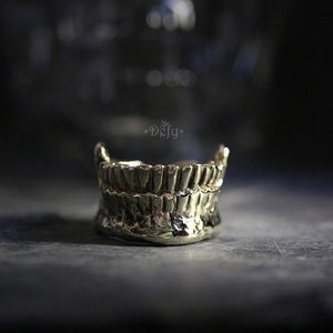 Puede incluir: Un anillo de color dorado con forma de dientes. El anillo está hecho de metal y tiene un diseño detallado.