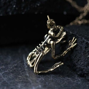 May include: A gold-toned pendant necklace featuring a detailed skeletal frog design. The pendant is hanging from a delicate chain.