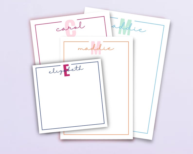 May include: A selection of personalised notepads featuring names in cursive writing. Each notepad has a coloured border and a matching initial. The names include Carol, Maddie, and Elizabeth. The notepads are white with coloured borders.
