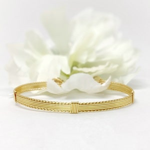 May include: A gold wire bracelet with a braided design. The bracelet is made of multiple strands of wire that are woven together to create a delicate and intricate pattern.