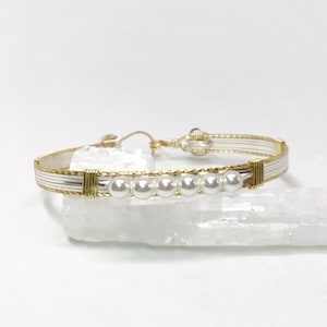 May include: A gold and silver wire wrapped bracelet with a row of white pearls.