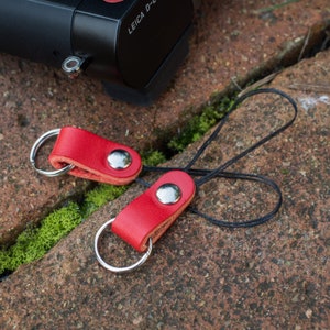 May include: Two red leather camera straps with silver metal rings and a black cord. The straps have a silver metal button.