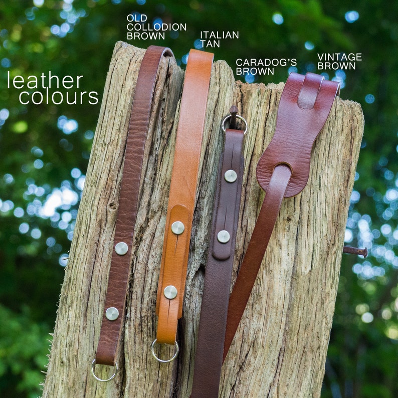 May include: Five leather camera straps in different shades of brown, including Old Collodion Brown, Italian Tan, Caradog's Brown, and Vintage Brown. The straps have silver metal accents and are displayed on a wooden surface.