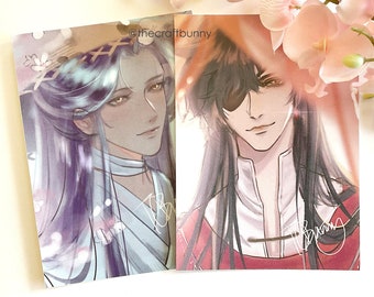 May include: Two illustrated prints of anime-style characters. The print on the left features a character with long blue hair and a white outfit. The print on the right features a character with black hair and a red outfit. Both characters have a similar expression and are looking to the right. The text "@thecraftbunny" is visible in the top right corner of the image.
