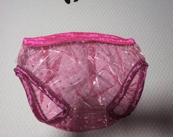 May include: A pair of translucent pink plastic underwear featuring a shiny, smooth texture. The garment is finished with a vibrant magenta satin-like trim along the waistband and the leg openings, providing a distinct contrast to the clear material.