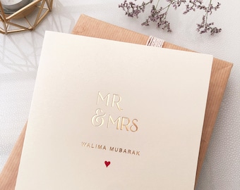 Può includere: Un biglietto bianco con lettere dorate in rilievo che recitano "MR & MRS" e "WALIMA MUBARAK". Un piccolo cuore rosso si trova sotto il testo.