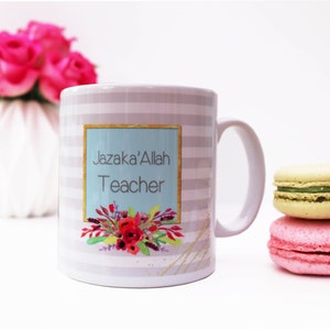 May include: White ceramic mug with a grey and white striped pattern. The mug features the text "Jazaka'Allah Teacher" on a teal background with floral accents. Pink roses and macarons are in the background.