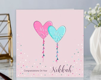 May include: Pink and blue heart shaped balloons with the words "Mrs" and "Mr" on them. The balloons are tied with strings of tassels. The background is pink with white and blue confetti. The text "Congratulations On Your Nikkah" is at the bottom of the card.