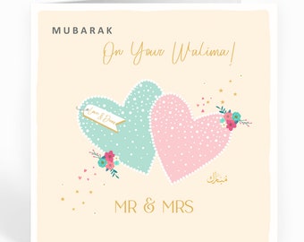 May include: A light peach card with a gold inscription that reads "Mubarak On Your Walima!" Two intertwined hearts, one light blue and one pink, are decorated with white dots and gold trim. The hearts are adorned with flowers and a banner that reads "Love & Dua's". The card also features gold stars and the text "MR & MRS" in gold.