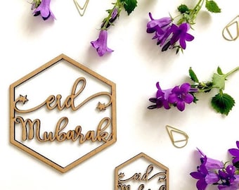 May include: Two wooden hexagonal signs with the text "Eid Mubarak" in a decorative script. The signs are on a white background with purple flowers.