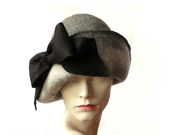 May include: A gray and black felt cloche hat with a large black bow. The hat is angled on a mannequin head.
