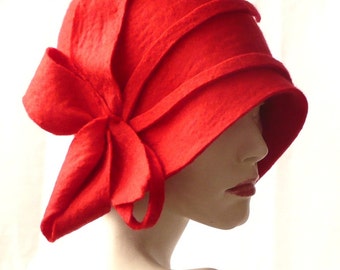May include: A red felt cloche hat with a large bow on the side. The hat has a wide brim and a fitted crown.