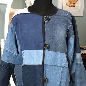 May include: A patchwork denim coat in various shades of blue. The coat features large black buttons, a black collar, and two front pockets. The coat is knee-length and has a unique, handcrafted appearance.