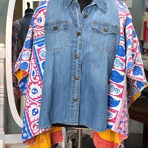 May include: A denim shirt with a colorful patterned fabric overlay. The shirt has a button-down front, two chest pockets, and long sleeves. The overlay features a mix of pink, blue, and yellow patterns, creating a unique and artistic look.