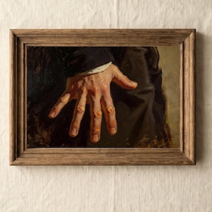 May include: A framed oil painting depicting a hand with prominent orange-toned knuckles and fingers resting against dark fabric. The hand is positioned centrally, showing detailed skin texture and shading. The artwork is enclosed in a rustic wooden frame.