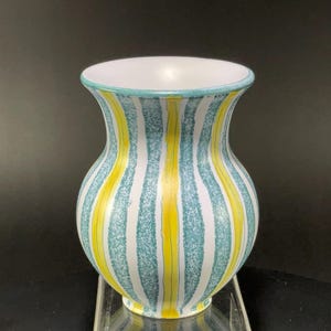 May include: A ceramic vase with a white interior and a turquoise rim. The exterior features vertical stripes in white, turquoise, and yellow. The vase has a rounded body and a flared opening.