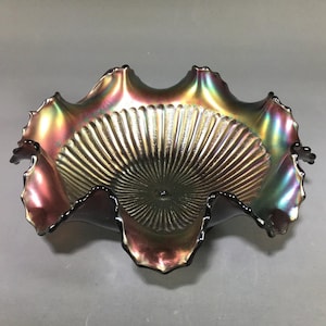 May include: An iridescent glass bowl with a ruffled rim and a textured, fan-like pattern in the center. The bowl has a dark, almost black, rim and displays a range of colors, including gold, purple, and green.
