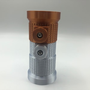 May include: A 3D-printed lightsaber hilt in bronze, silver, and brown. The hilt has a textured grip and two circular accents with screws. The top section is bronze, the middle section is brown, and the bottom is silver.