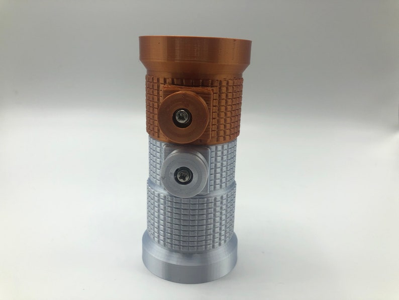 May include: A 3D-printed lightsaber hilt in bronze, silver, and brown. The hilt has a textured grip and two circular accents with screws. The top section is bronze, the middle section is brown, and the bottom is silver.