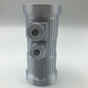 May include: A cylindrical, gray 3D-printed object with a textured surface and two circular attachments secured by screws. The object has a flared top and base, and the textured pattern covers the central portion.