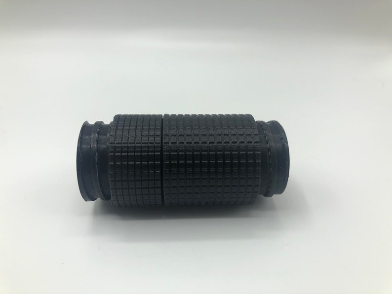 May include: A black, cylindrical object with a textured, grid-like pattern. The object appears to be made of plastic or a similar material. It has a series of ridges and grooves at each end, and is approximately 6 inches long.