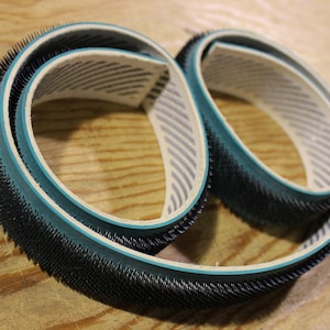 May include: Two black and green sanding belts with a white and gray striped lining. The belts are made of a soft, flexible material and have a textured surface.