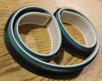 May include: Two black and green sanding belts with a white and gray striped lining. The belts are made of a soft, flexible material and have a textured surface.