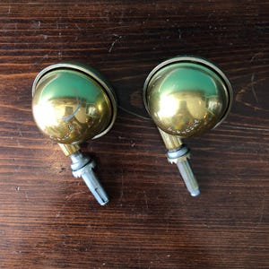 May include: Two spherical brass furniture castors with a polished finish. Each castor features a rounded wheel housing, a metal mounting stem, and the word Shepherd embossed on the surface of the brass sphere, indicating the brand name.