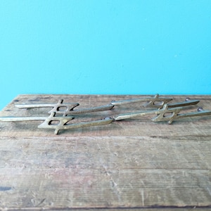 Peut inclure: Quatre poignées de tiroir en laiton antique avec un motif géométrique. Les poignées sont disposées en quinconce sur une surface en bois.