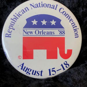 Könnte beinhalten: Ein weißer Knopf mit blauem und rotem Text und einem roten Elefantenlogo. Der Text lautet "Republican National Convention New Orleans '88 August 15-18".
