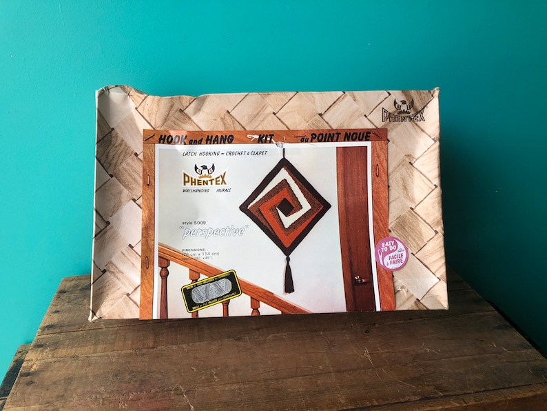 May include: A brown and white latch hook kit with a square design and a tassel. The kit is called "Perspective" and is made by Phentex. The box is labeled "Hook and Hang Kit" and "au Point Noue".