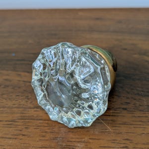 Peut inclure: Un bouton de porte en verre clair et facetté avec une base dorée. Le bouton a une forme arrondie et une surface texturée, reflétant la lumière. Ce bouton de porte de style vintage est adapté à la décoration intérieure.