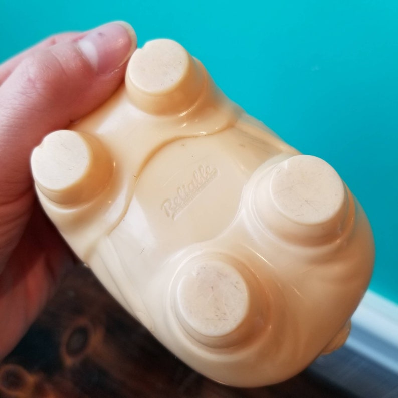 May include: A cream-coloured plastic piggy bank with four feet and the word "Reliable" printed on the bottom.