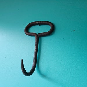 May include: A rusty metal hook with a rounded handle hangs on a turquoise wall.