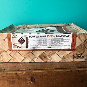 May include: A brown cardboard box with a woven pattern. The box contains a "Hook and Hang Kit du Point Noue" craft kit. The kit includes all the materials needed to create a wall hanging. The box features a picture of the finished product, a geometric design with a spiral pattern. The text on the box reads "Style 5009" and "Perspective".
