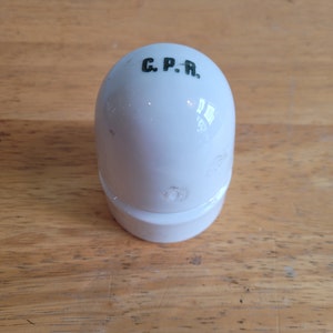 Può includere: Tappatore per bottiglia in ceramica bianca a forma di uovo con la scritta "C.P.R." stampata sulla parte superiore.