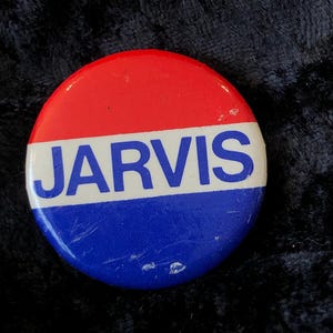 Könnte beinhalten: Ein roter, weißer und blauer Knopf mit dem Wort "JARVIS" in blauen Buchstaben.