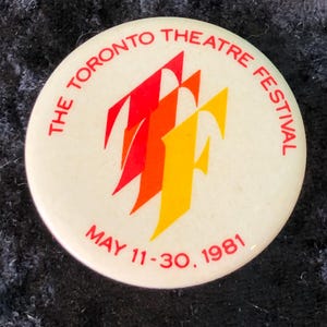 Könnte beinhalten: Ein runder, cremefarbener Knopf mit dem Text "THE TORONTO THEATRE FESTIVAL" in Rot. Der Knopf zeigt ein stilisiertes Logo in Rot, Orange und Gelb, mit den Daten "MAY 11-30, 1981" in Rot.