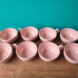 May include: Set of eight pink ceramic teacups. The cups are all the same size and shape, and they have a smooth, glossy finish.