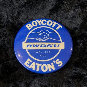 Könnte beinhalten: Blau-weißer Knopf mit dem Text "Boycott RWDSU AFL-CIO CLC Eaton's" und einer Handshake-Grafik.