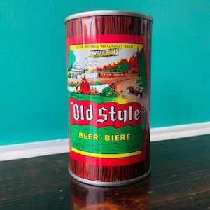 May include: A vintage Old Style Beer can with a red and brown woodgrain design. The label features a green banner with "BEER - BIERE" and a scenic illustration. The can is 355 ml and 5% alc/vol.