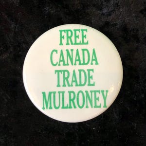 Könnte beinhalten: Ein weißer Knopf mit grünem Text, der "FREE CANADA TRADE MULRONEY" lautet.