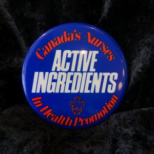 Könnte beinhalten: Ein blauer Knopf mit dem Text "Canada's Nurses Active Ingredients in Health Promotion" in weißer und roter Schrift. In der Mitte befindet sich ein kanadisches Ahornblatt.