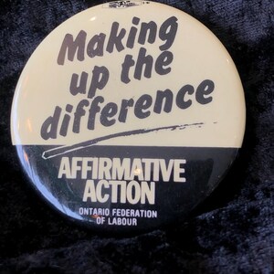 May include: A white and black button with the text "Making up the difference" and "Affirmative Action" with the text "Ontario Federation of Labour" below.