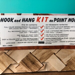 May include: A brown and tan cardboard box with a colorful image of a woven basket. The box is labeled "HOOK and HANG KIT au POINT NOUE" and lists the contents of the kit, including a full color design printed on canvas, yarn, and instructions. The box is made in Canada.