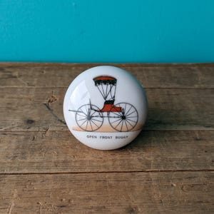 Peut inclure: Bouton en céramique blanche avec une image peinte à la main d'une calèche à ciel ouvert. Le texte "OPEN FRONT BUGGY" est imprimé sous l'image.