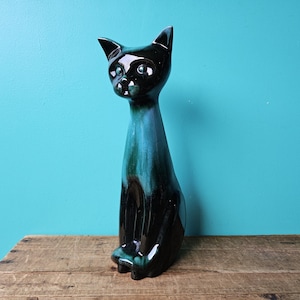 Pode incluir: Uma figura de gato de cerâmica esmaltada em preto e turquesa. O gato está sentado com o rabo enrolado em torno das suas pernas.