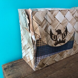 May include: A brown cardboard box with a woven pattern and a black eagle logo. The box is slightly damaged and has a blue mesh panel.