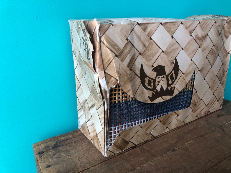 May include: A brown cardboard box with a woven pattern and a black eagle logo. The box is slightly damaged and has a blue mesh panel.