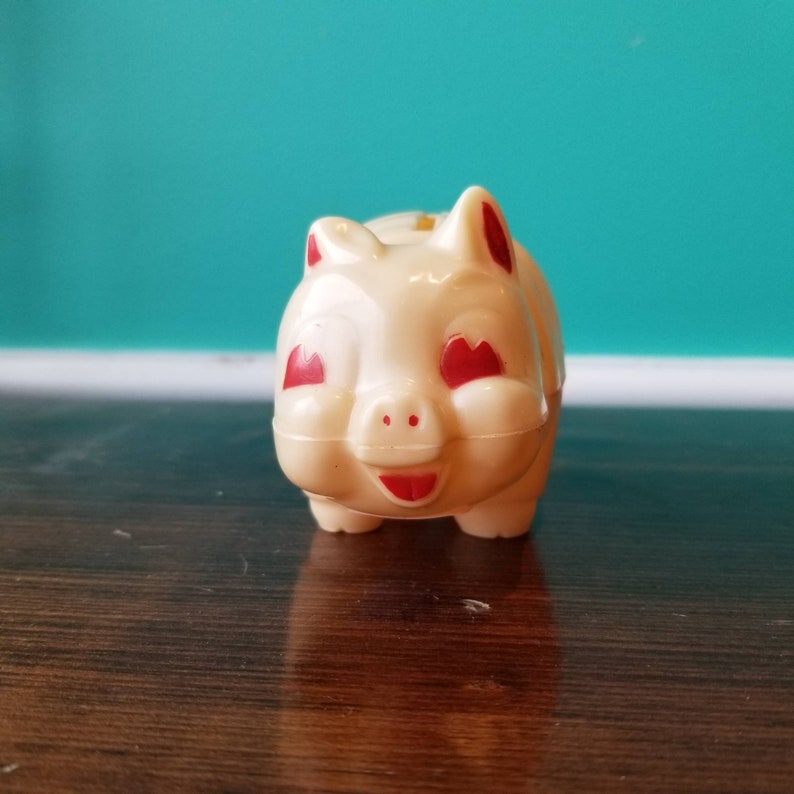 May include: A white plastic piggy bank with red heart-shaped eyes and a red smiling mouth.